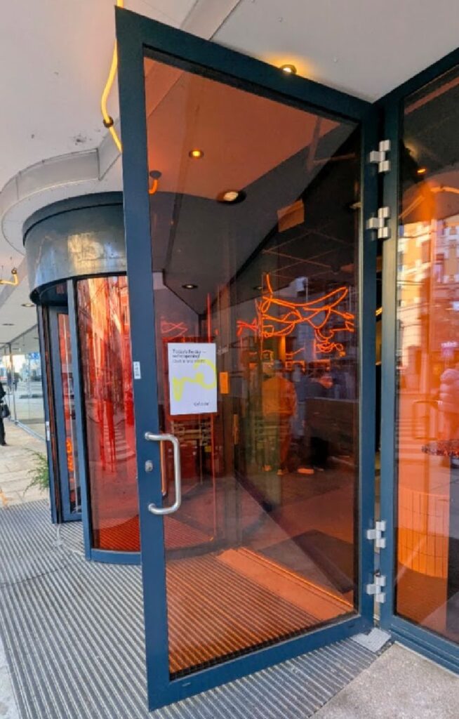 Hovedinngangen til Scandic GO i Grensen med oransje glassflater og plakat som markerer åpningsdagen.