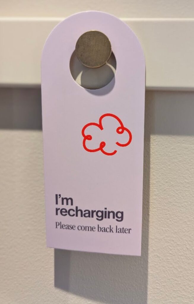 Hvitt dørskilt på Scandic GO med rød sky-logo og teksten «I’m recharging – Please come back later».