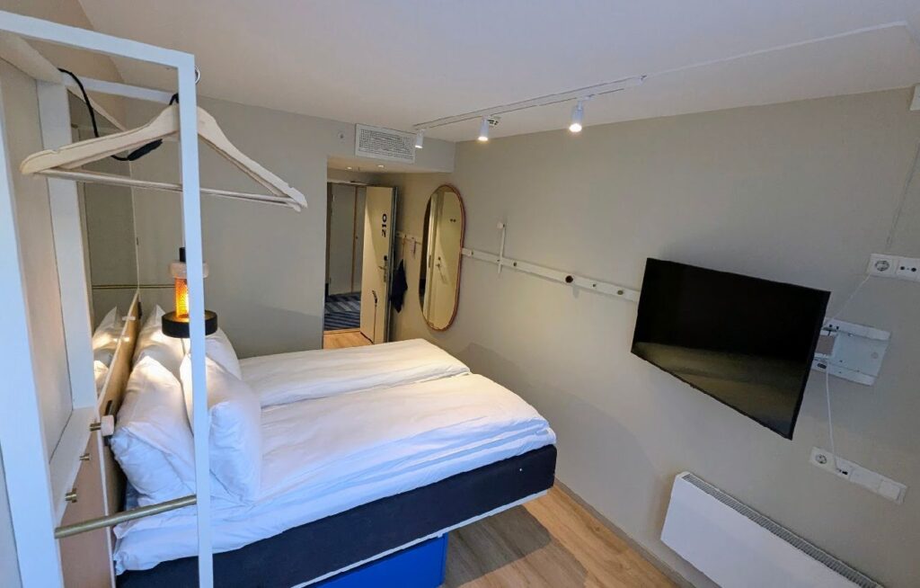 Moderne og arealeffektivt dobbeltrom hos Scandic GO i Grensen med smart-TV, åpen klesoppbevaring og lyst interiør.