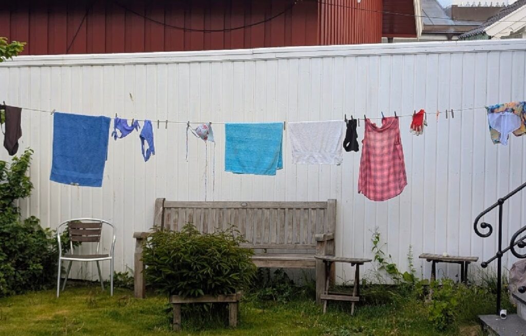 Håndklær og badetøy henger til tørk på snoren i en koselig, skjermet hage.