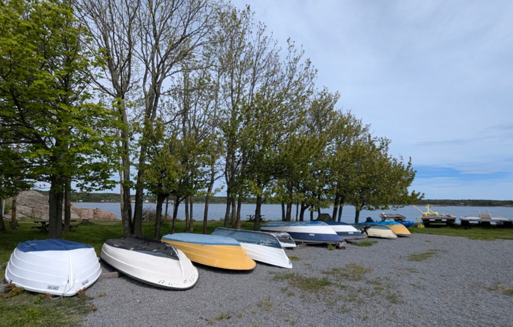 Rekke med småbåter trukket opp på land ved Nevlunghavn med fjorden i bakgrunnen