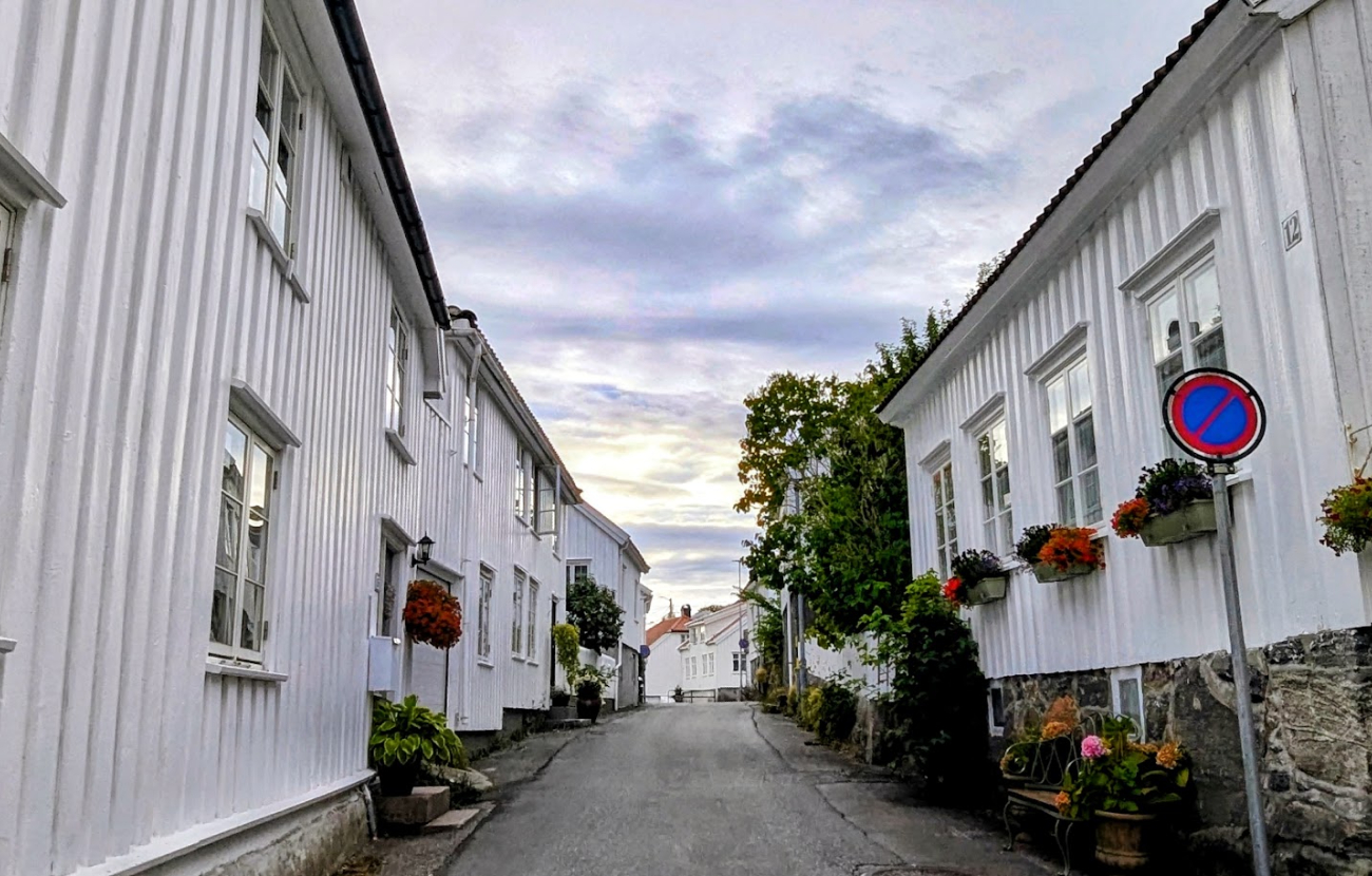 En smal gate i Grimstad med hvitmalte trehus med blomster.