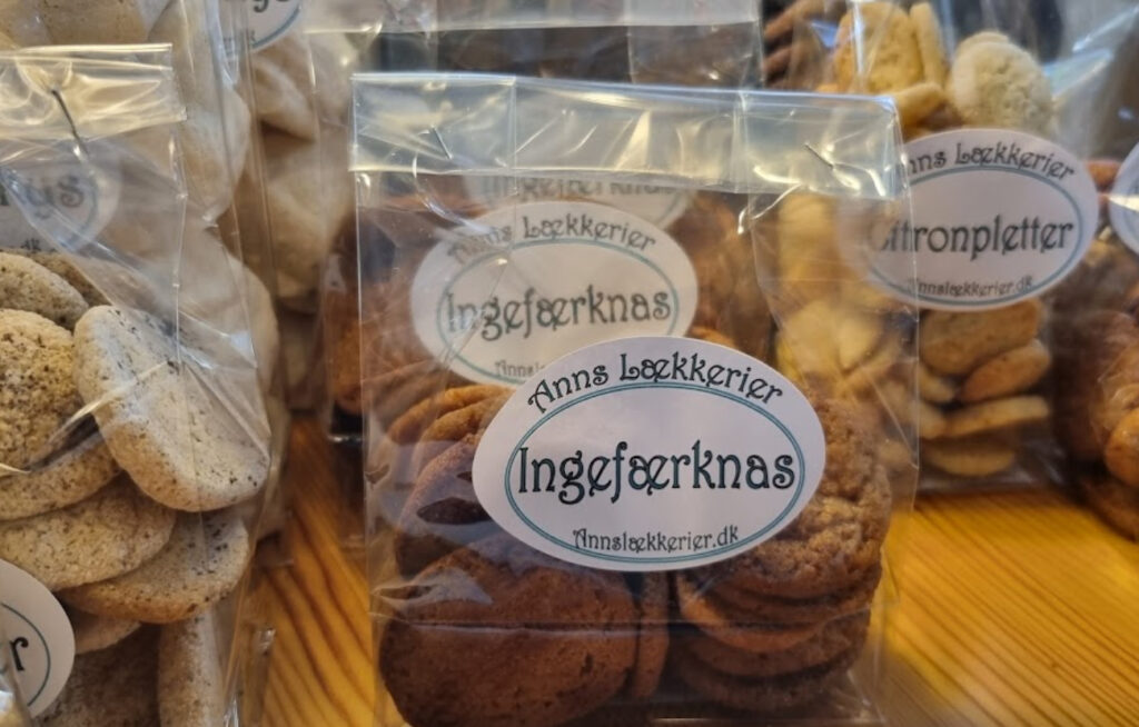 Gjennomsiktige poser med sprø, hjemmebakte kjeks merket med etiketten «Ingefærknas» og «Citronpletter» fra Anns Lækkerier, oppstilt på en treflate.